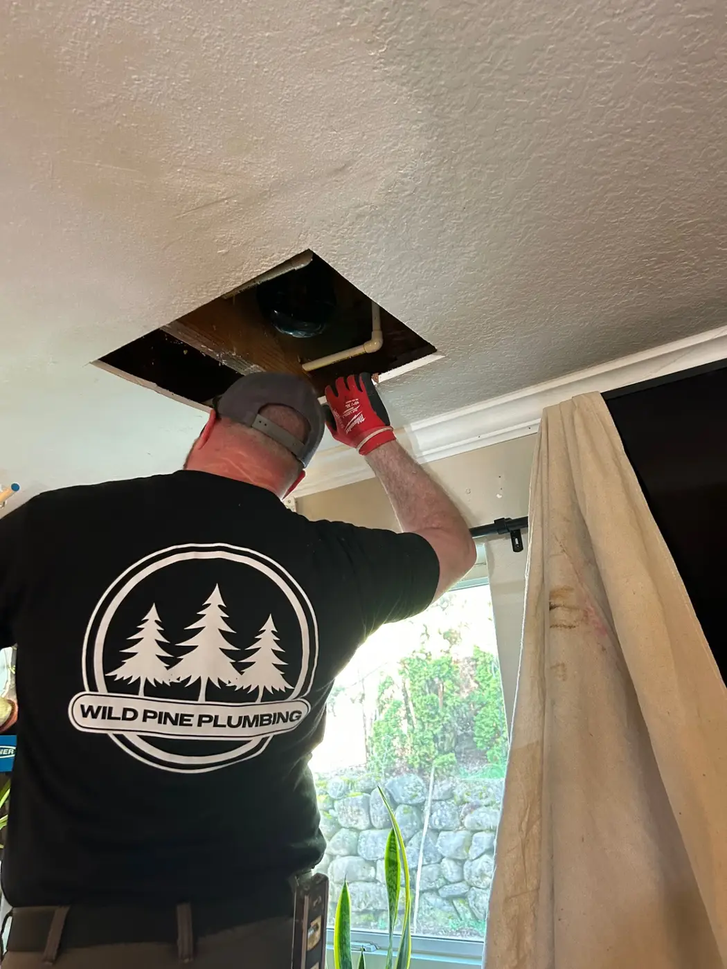 Wild Pine Plumbing technician repairing a drain line through a ceiling access in a Portland, Oregon home