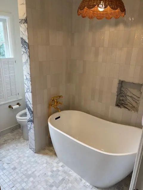 Freestanding soaking tub with brushed gold tub filler and zellige tile surround by Wild Pine Plumbing in Portland, OR