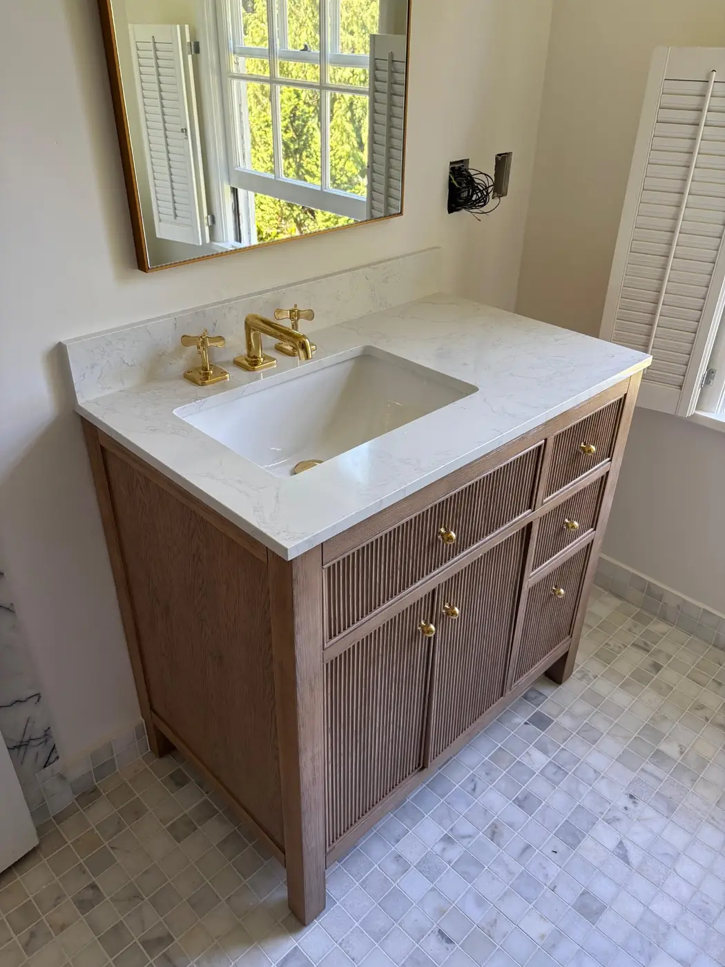 Oak fluted vanity with quartz marble top and brushed gold cross-handle faucet installed by Wild Pine Plumbing in Portland, Oregon